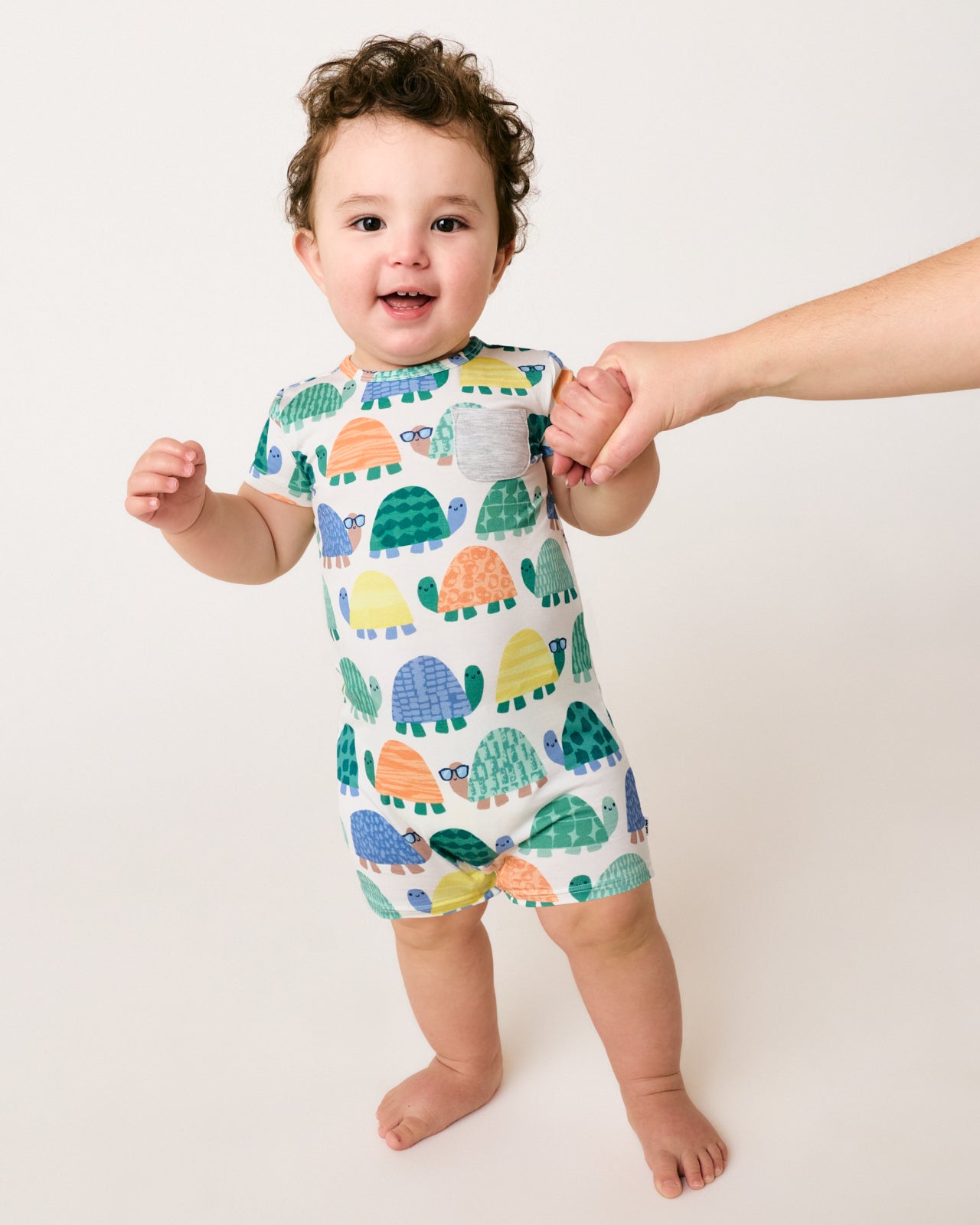 Standing baby wearing the Shell Parade Pocket Shorty Romper