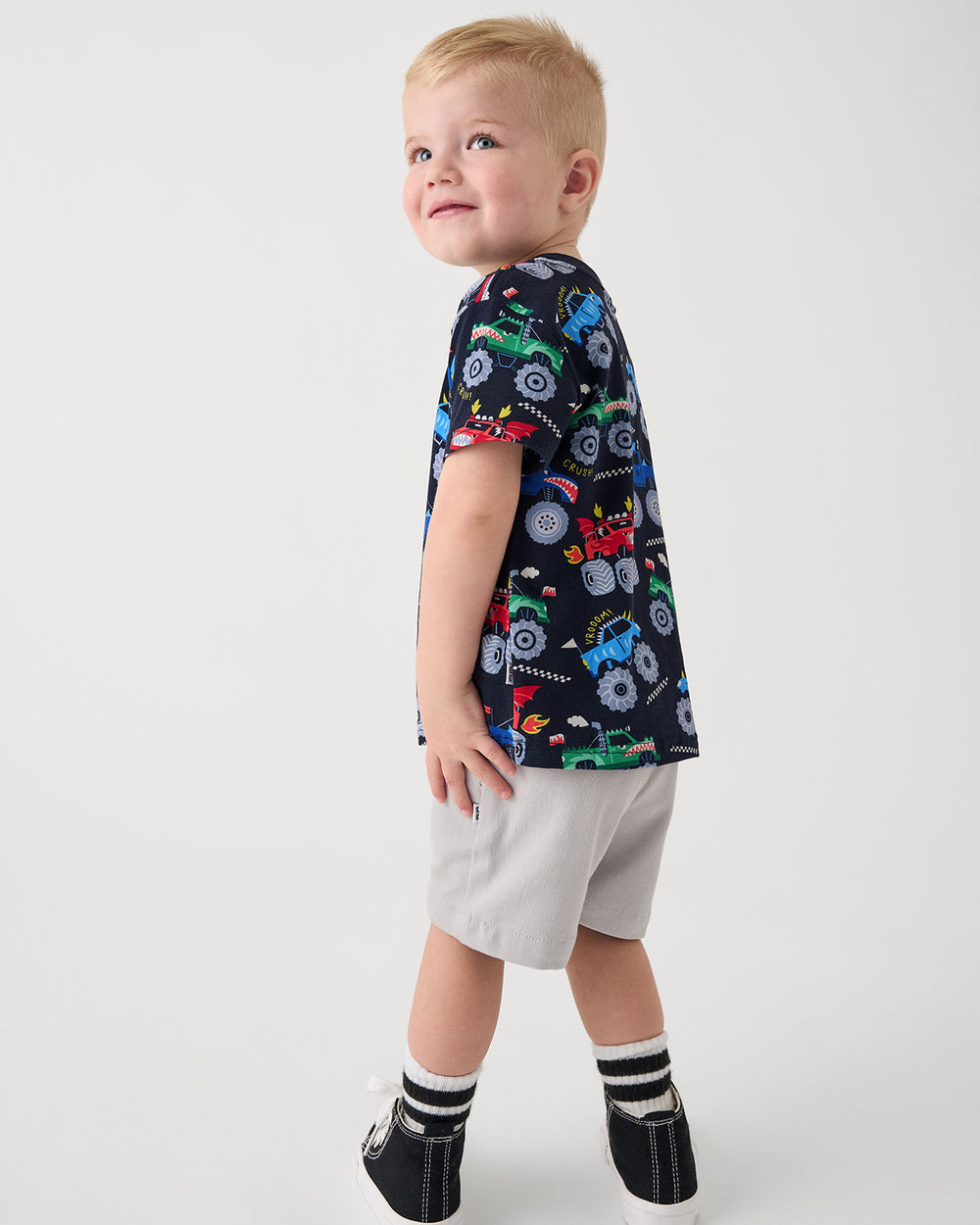 Standing child wearing the Monster Truck Madness Relaxed Tee with gray boys shorts