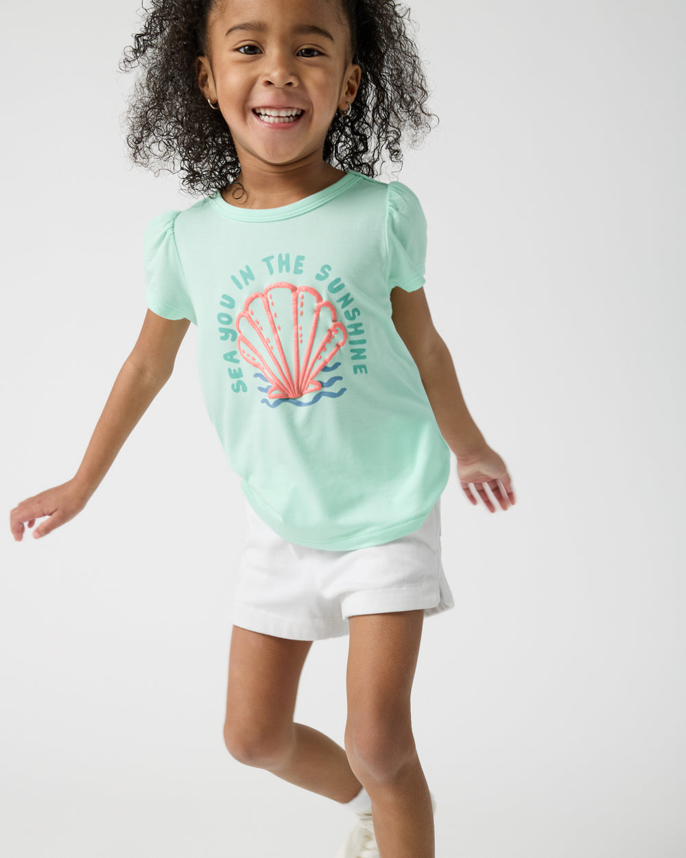 Girl wearing the Sparkling Seas Puff Sleeve Tee and white denim shorts