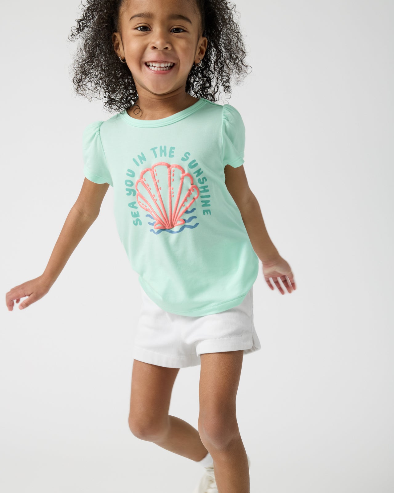 Girl wearing the Sparkling Seas Puff Sleeve Tee and white denim shorts