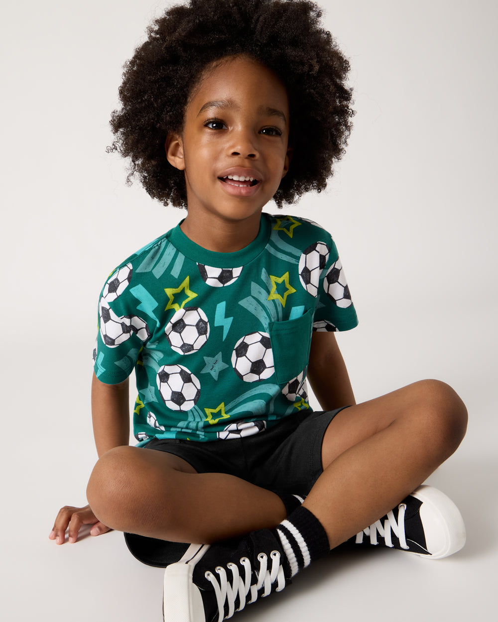Sitting boy wearing the Soccer Stars Relaxed Pocket Tee with lace up sneakers