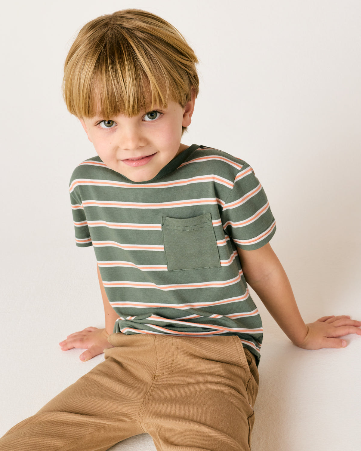 Sitting boy wearing the Moss Stripe Relaxed Pocket Tee with khaki pants