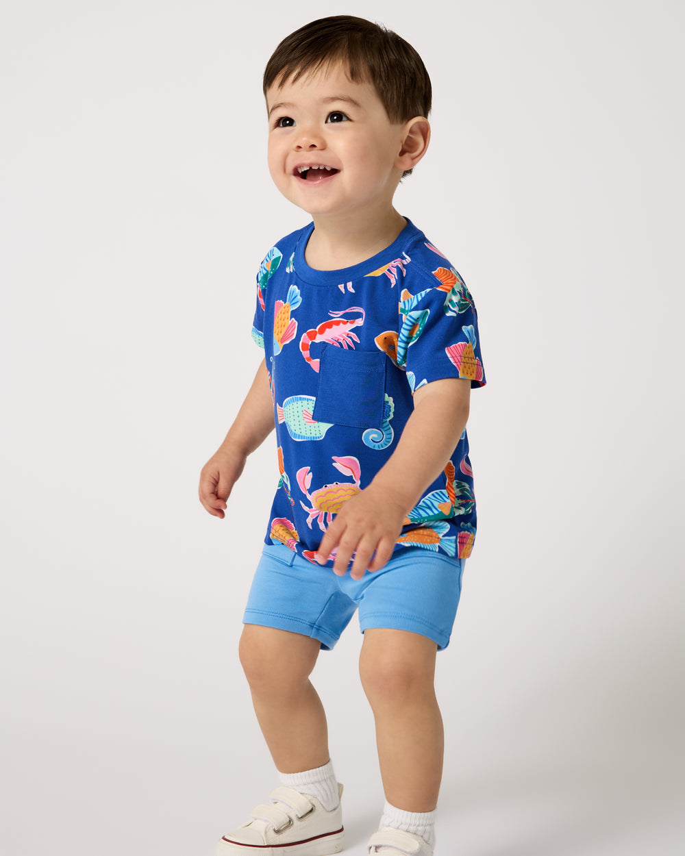 Boy wearing the Tidepool Party Relaxed Pocket Tee with blue boys shorts