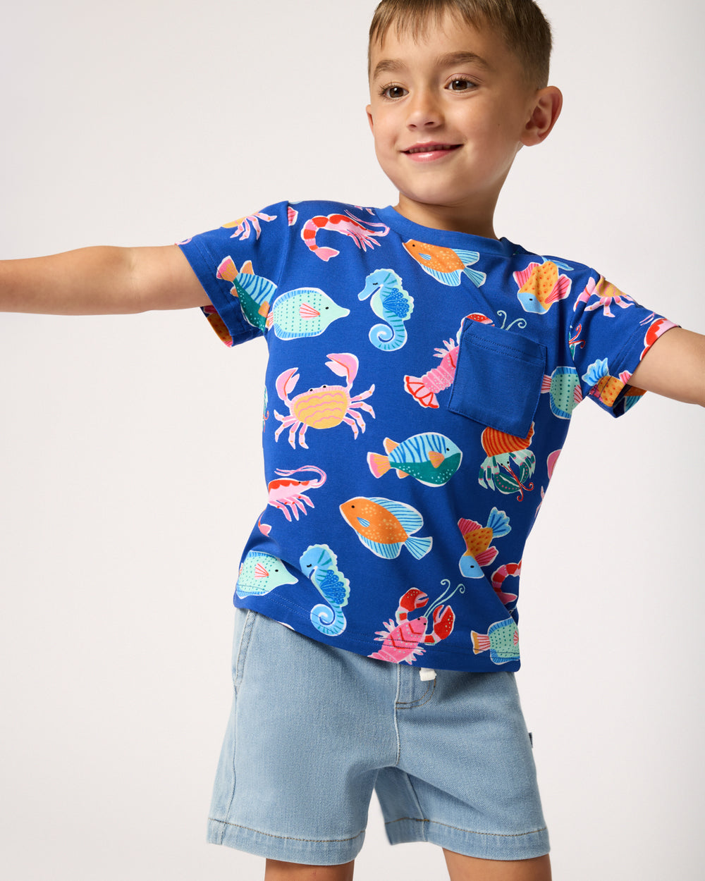 Boy wearing the Tidepool Party Relaxed Pocket Tee with denim chino shorts