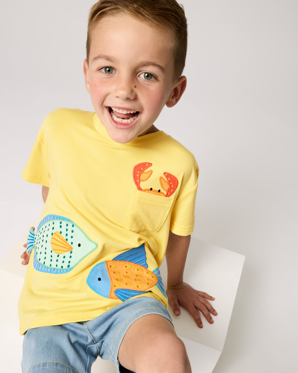 Sitting child wearing the School of Friends Relaxed Pocket Tee with denim chino shorts