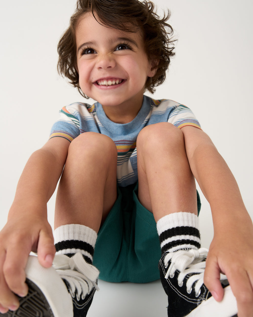 Sitting child wearing the Explorer Stripes Relaxed Pocket Tee with black sneakers