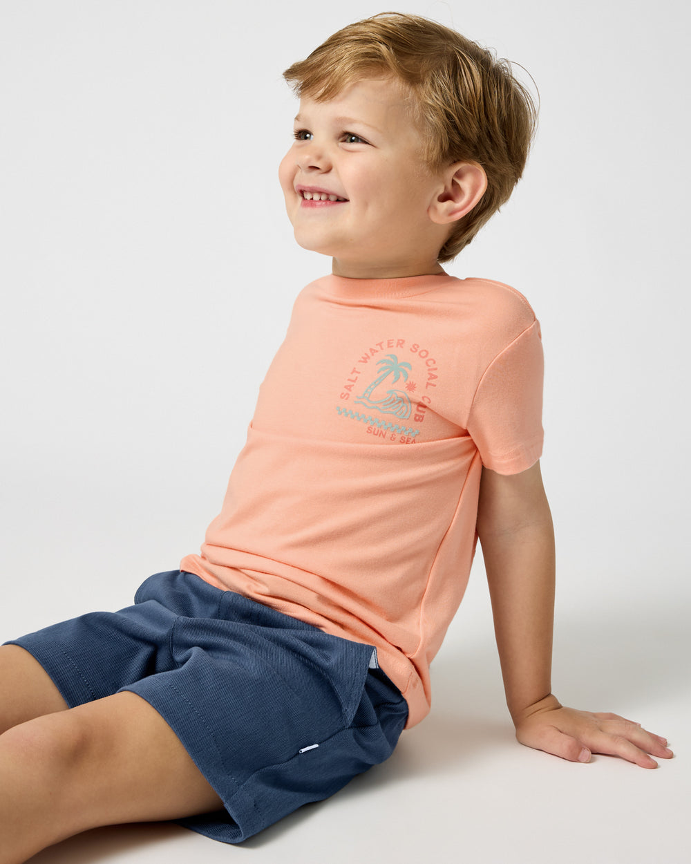 Sitting boy wearing the Salt Water Social Club Relaxed Tee with Vintage Navy Chino Shorts