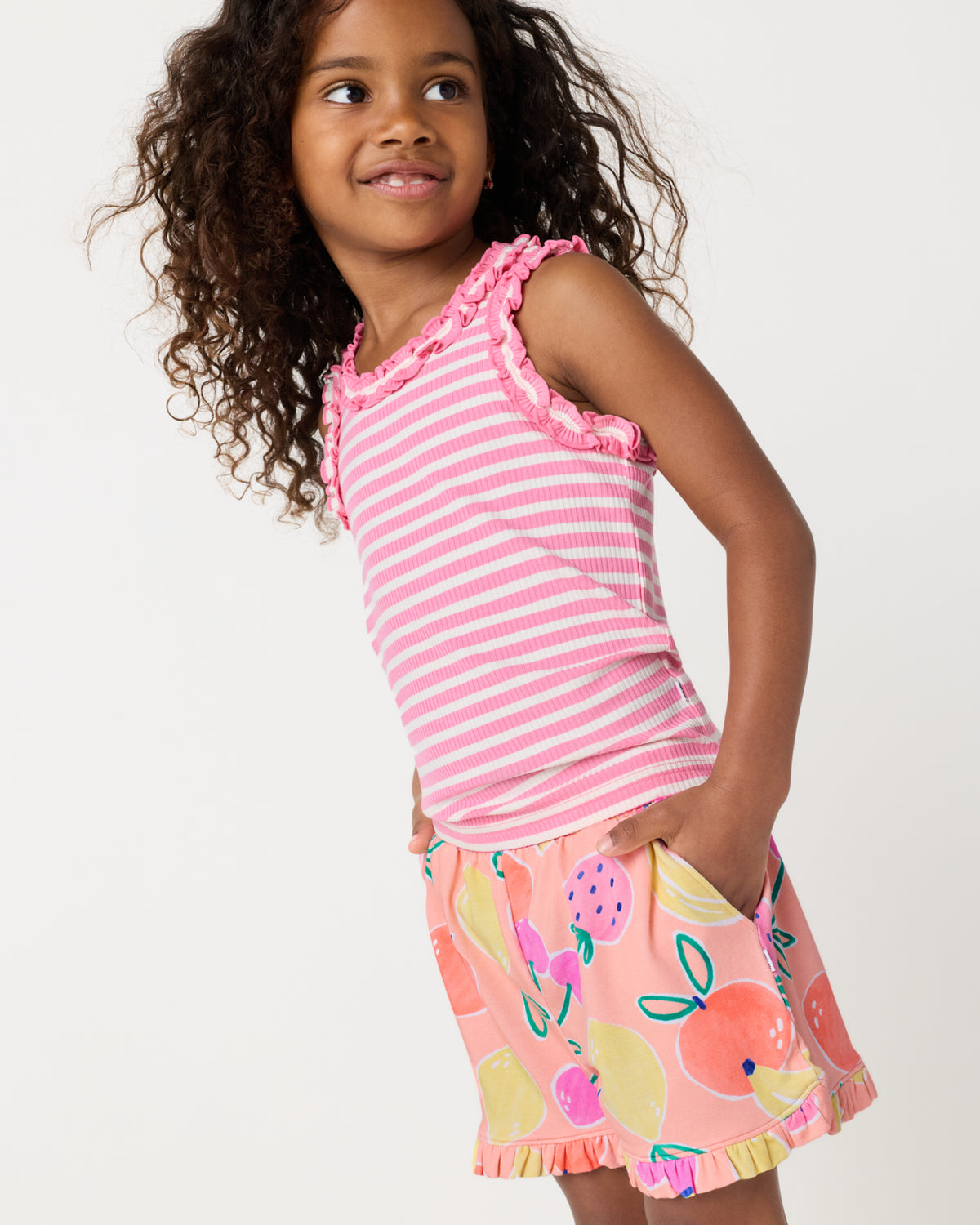 Girl wearing the Sweet Pink Stripe Ruffle Tank with fruit print shorts