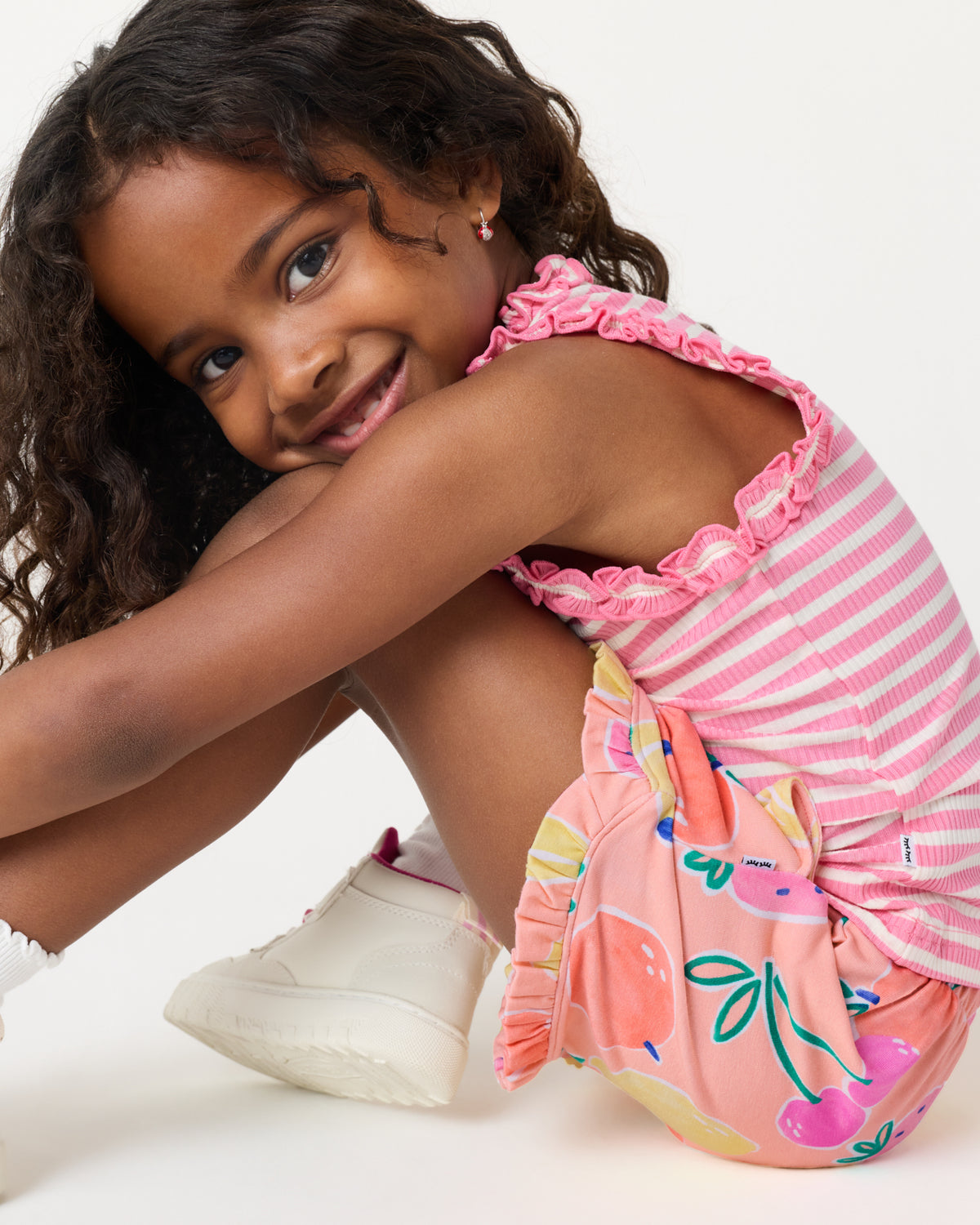 Sitting girl wearing the Sweet Pink Stripe Ruffle Tank and Fruit Frenzy Ruffle Shorts