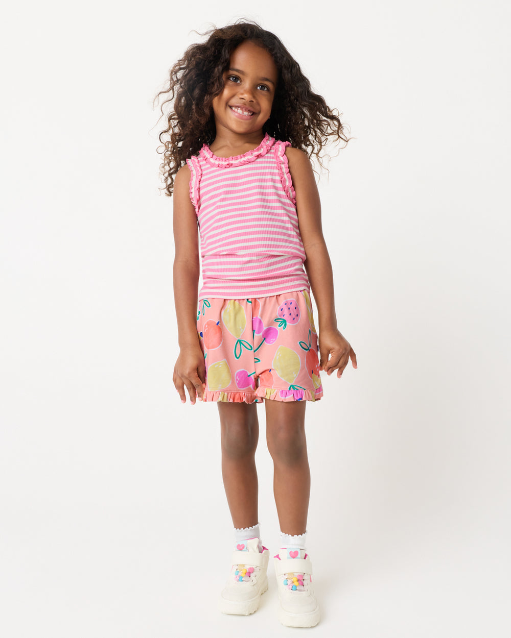 Standing girl wearing the Sweet Pink Stripe Ruffle Tank with fruit printed ruffle shorts