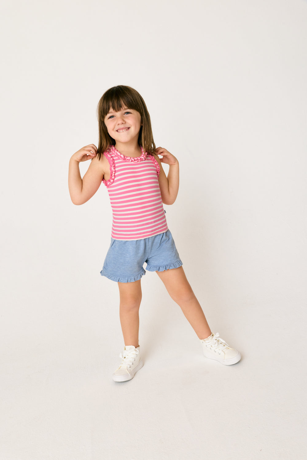 Standing girl wearing the Heather Blue Ruffle Shorts and Pink Stripe Ruffle Tank