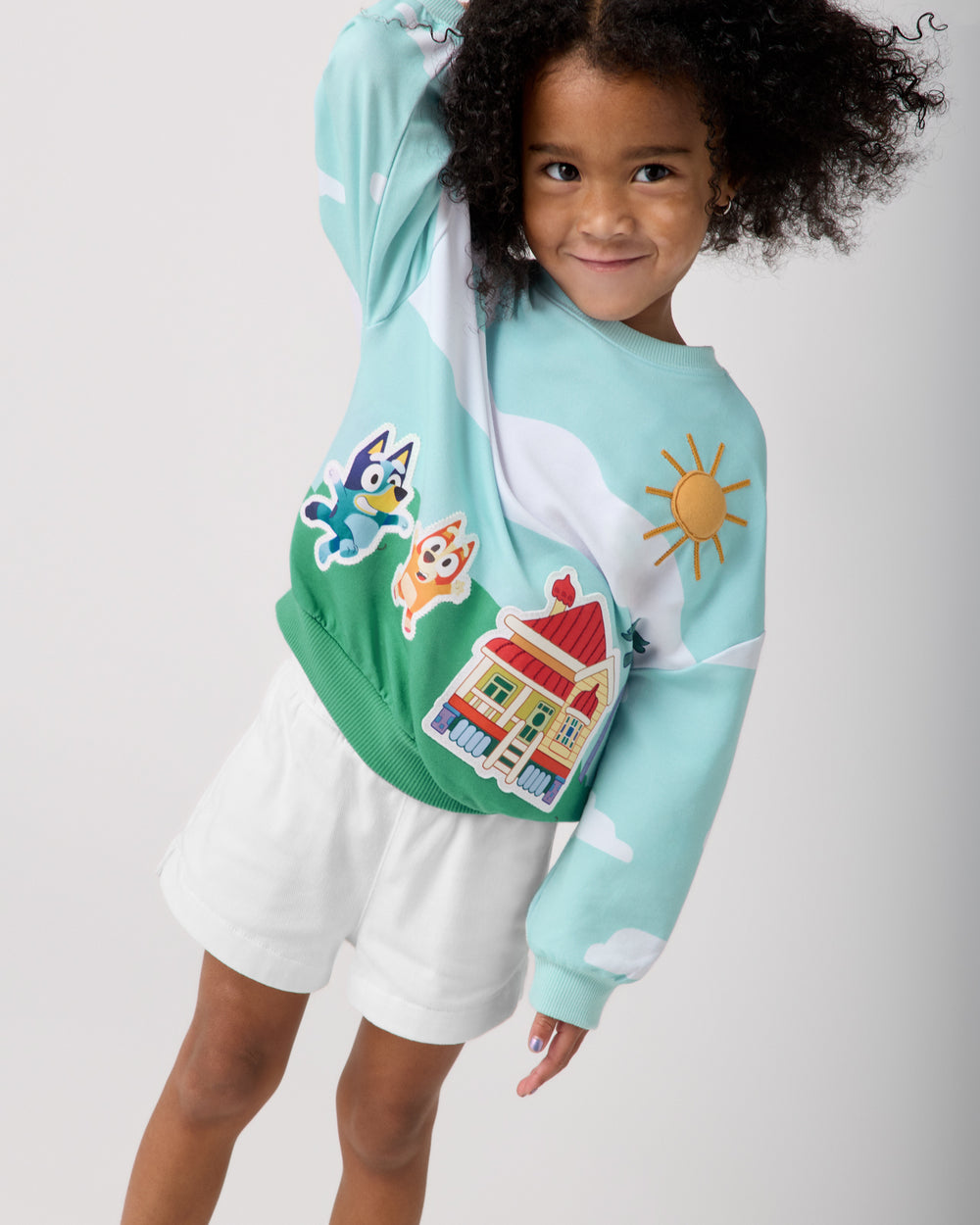 Girl wearing the Bluey The Heeler House Drop Shoulder Crewneck with white denim shorts