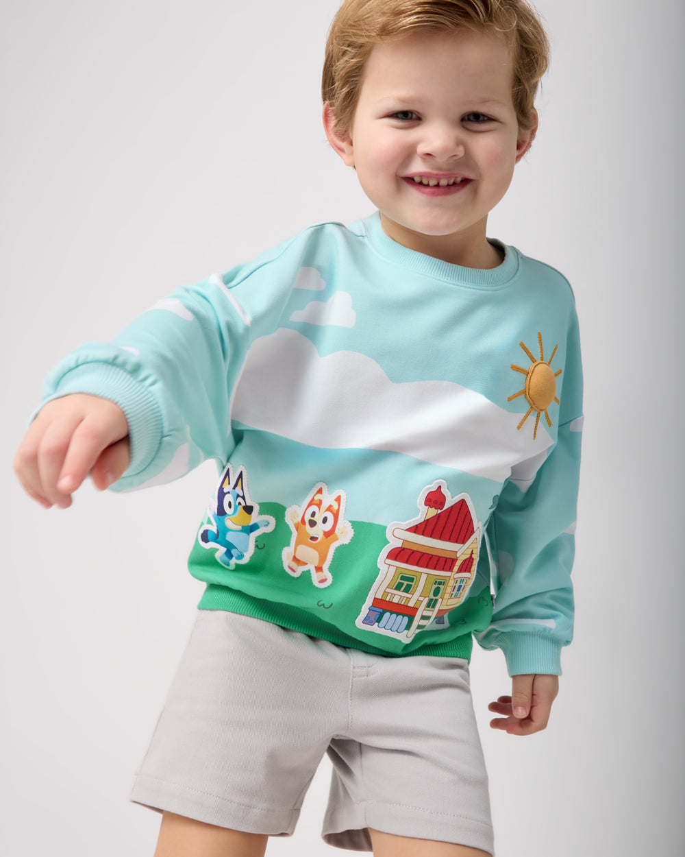 Boy wearing the Bluey The Heeler House Drop Shoulder Crewneck with gray chino shorts