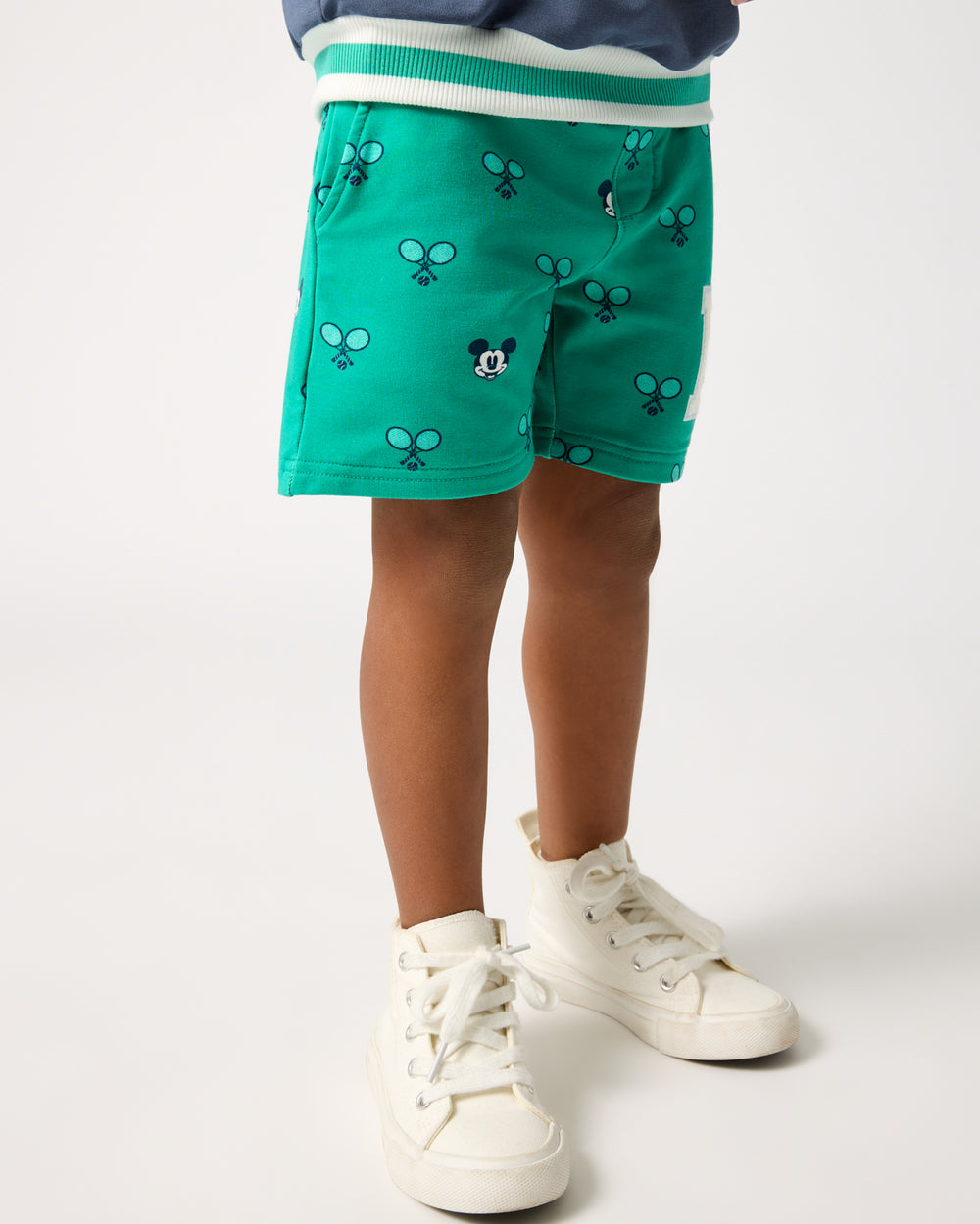 Boy wearing the Disney Mickey Mouse Racket Rally Drawstring Shorts with white sneakers