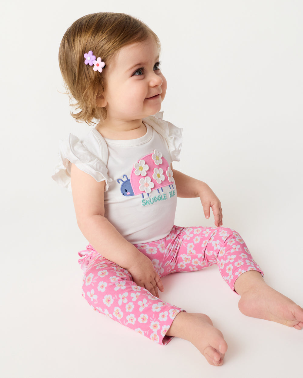 Sitting baby wearing the Sweet Pink Petals Ruffle Legging with the coordinating Snuggle Bug Flutter Bodysuit