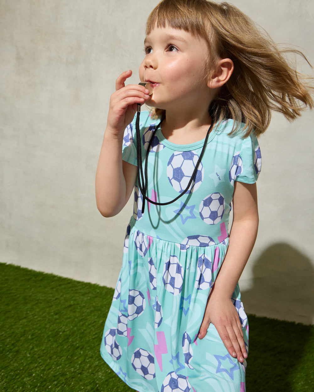Child wearing the Aqua Soccer Stars Skater Dress with a whistle 