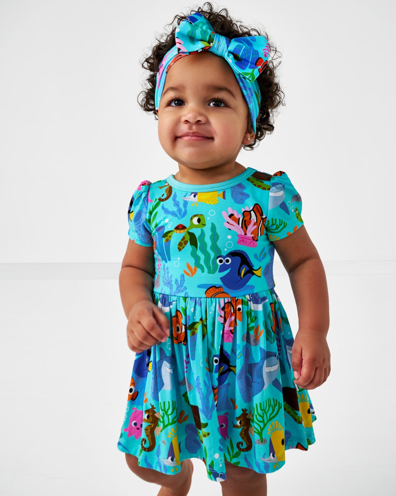 Close up of toddler wearing the Disney Nemo's Reef Skater Dress with Bodysuit and the matching luxe bow headband