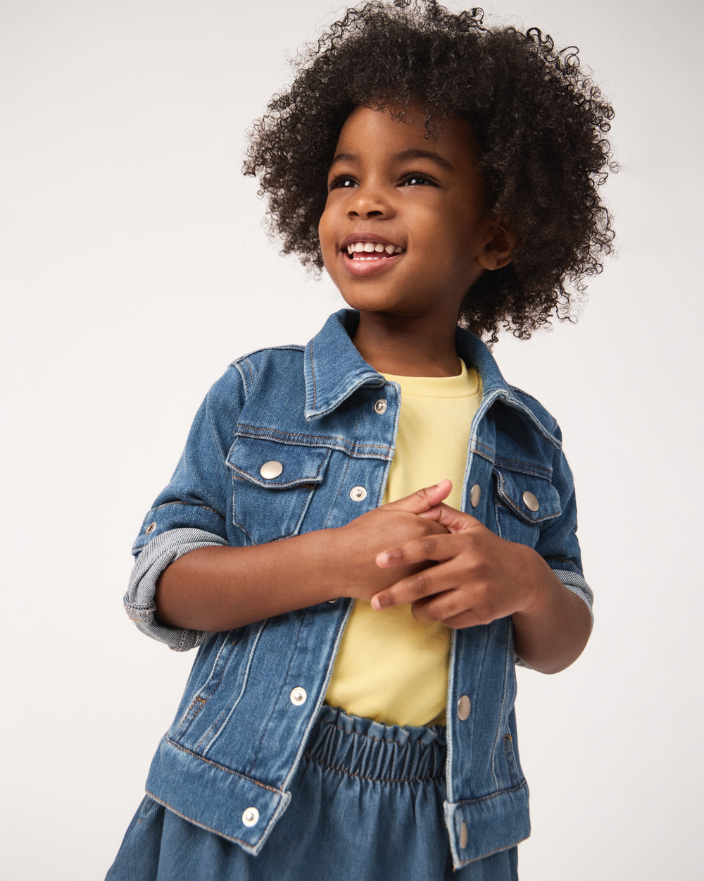 Girl wearing the Midwash Blue Denim Trucker Jacket layered over a yellow shirt