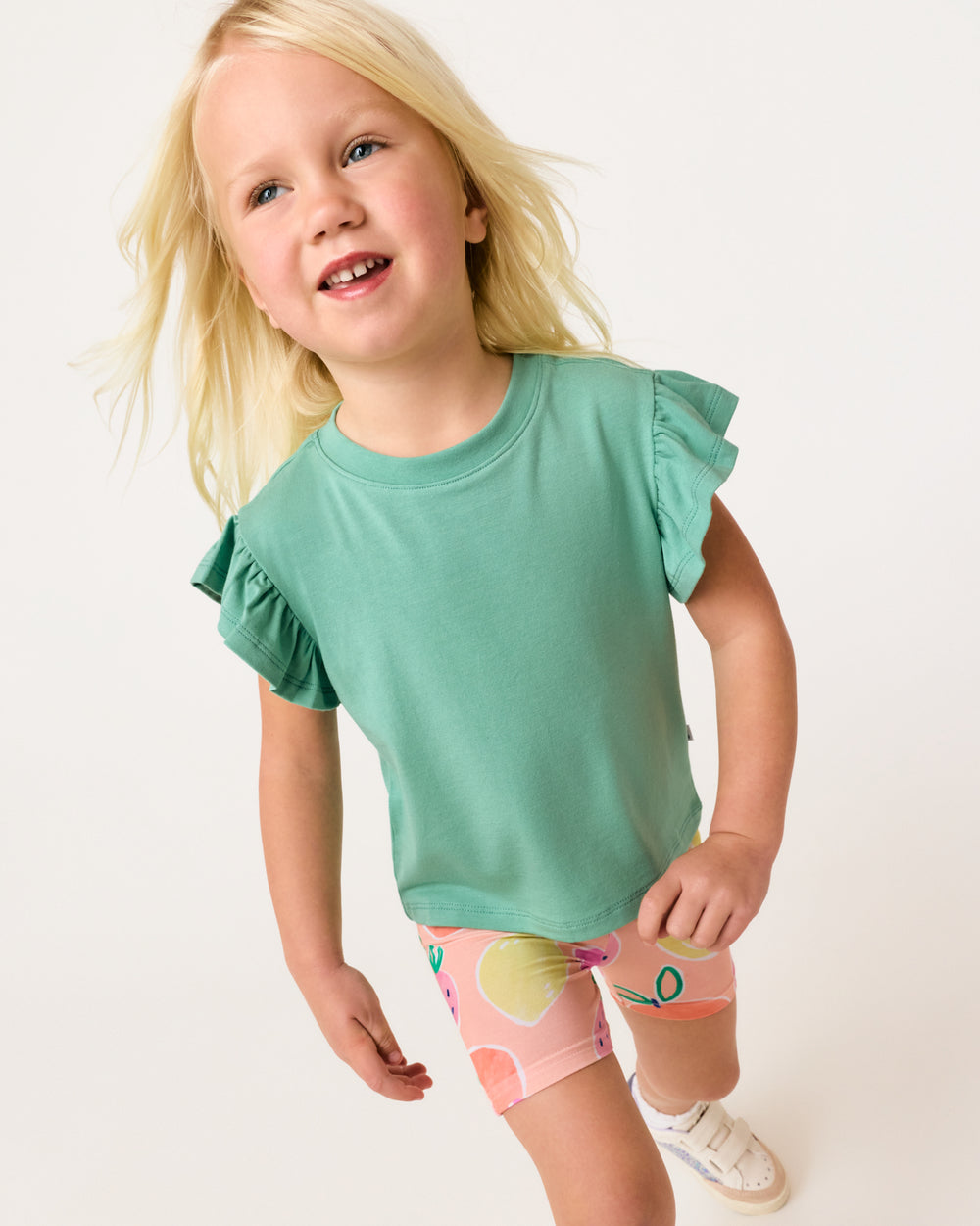 Walking girl wearing the Cool Jade Flutter Tee with fruit print shorts