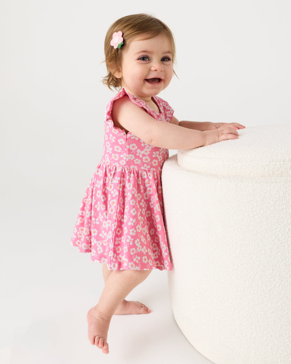 Baby holding onto an ottoman wearing the Sweet Pink Petals Flutter Twirl Dress with Bodysuit