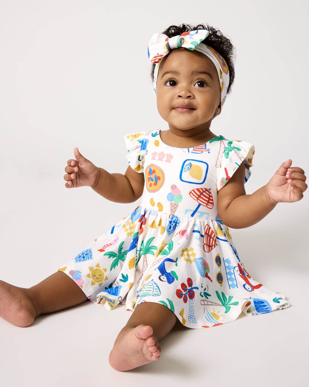 Sitting baby wearing the Ciao Bella Twirl Dress with Bodysuit and Luxe Bow Headband