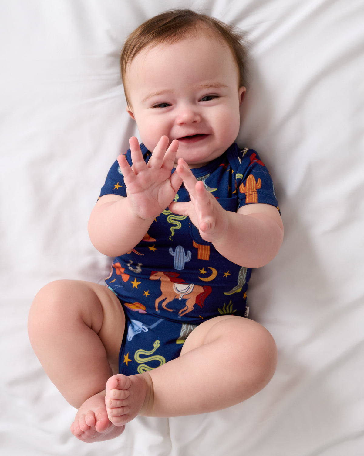Baby laying on a white blanket wearing the Blue Rancher Roundup Pocket Bodysuit 