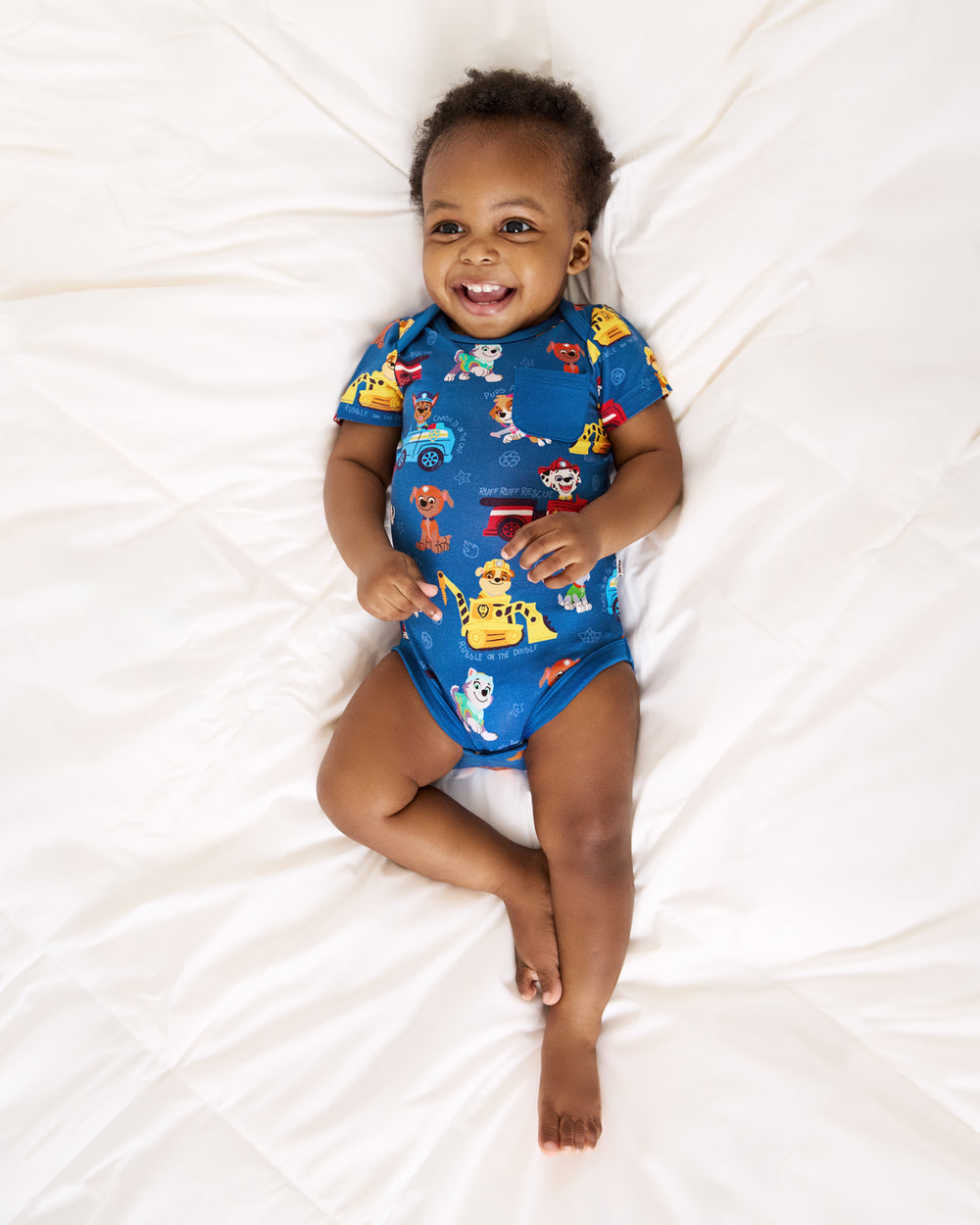 Baby laying on a bed wearing the PAW Patrol Adventure Bay Heroes Pocket Bodysuit