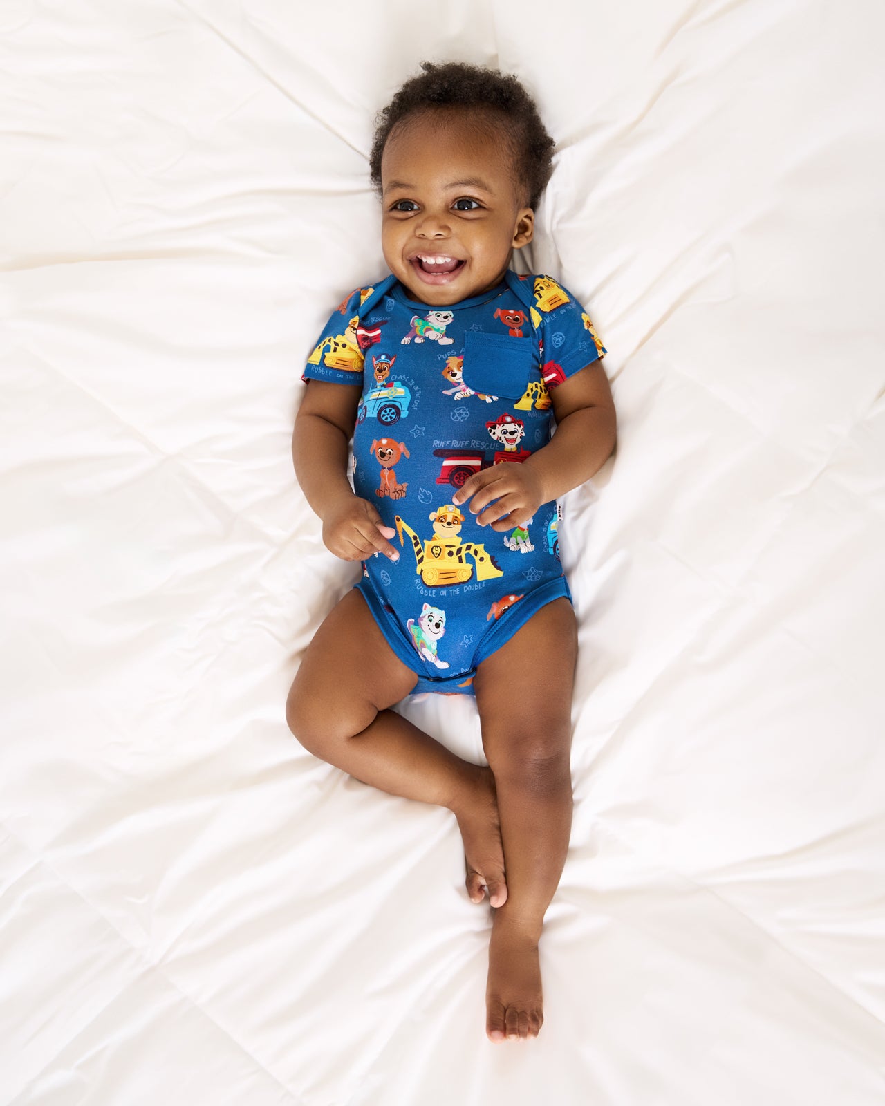 Baby laying on a bed wearing the PAW Patrol Adventure Bay Heroes Pocket Bodysuit