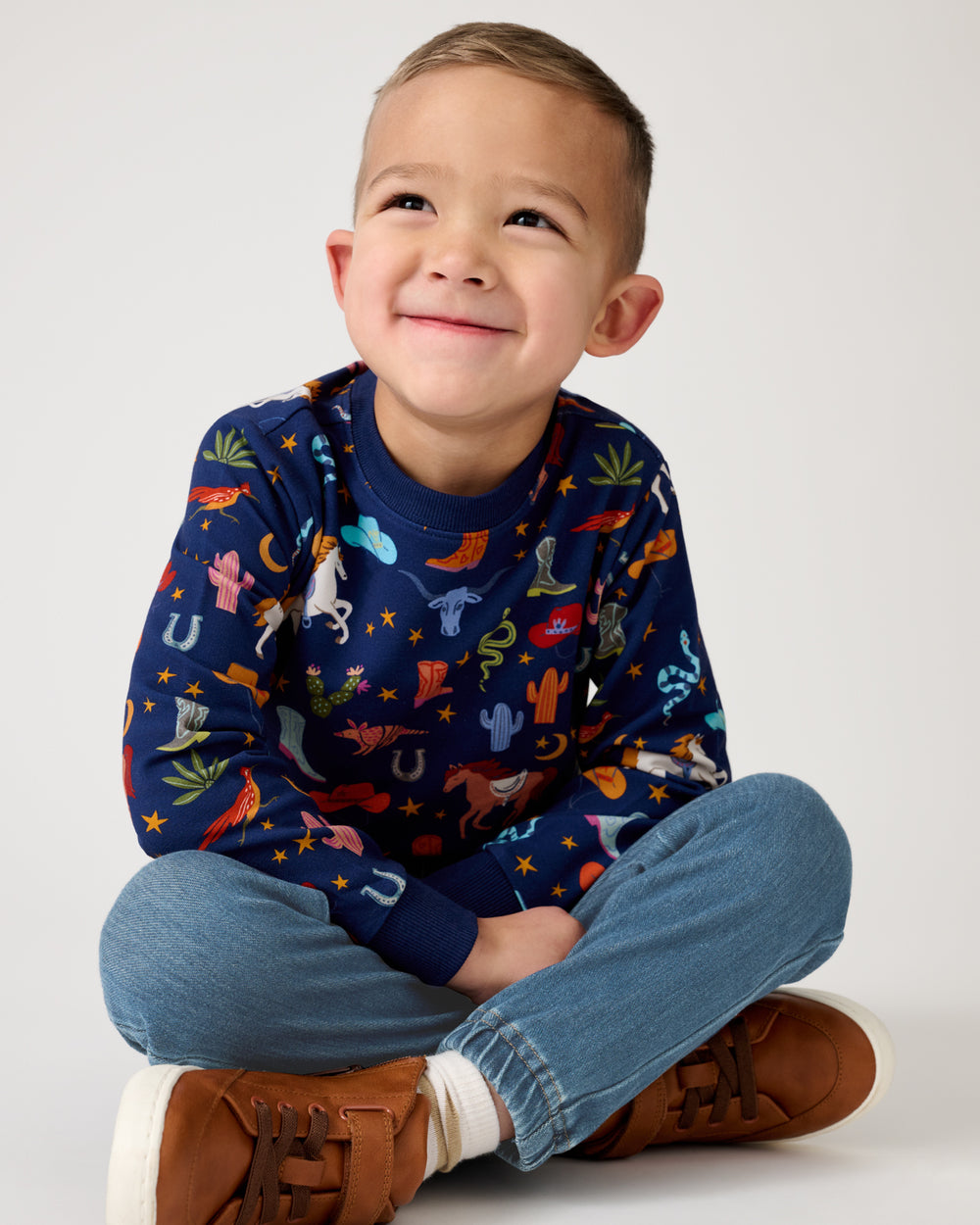 Sitting child wearing the Blue Rancher Roundup Crewneck Sweatshirt and denim joggers