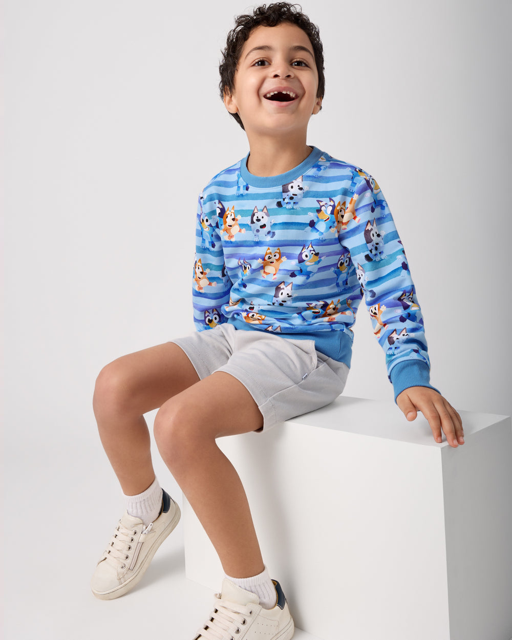 Sitting boy wearing the Bluey Dance All Day Crewneck Sweatshirt with gray boys shorts