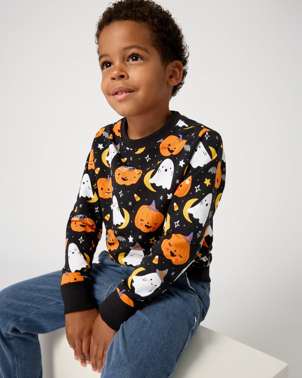 Sitting boy wearing the Moonlit Magic Crewneck Sweatshirt and denim pants