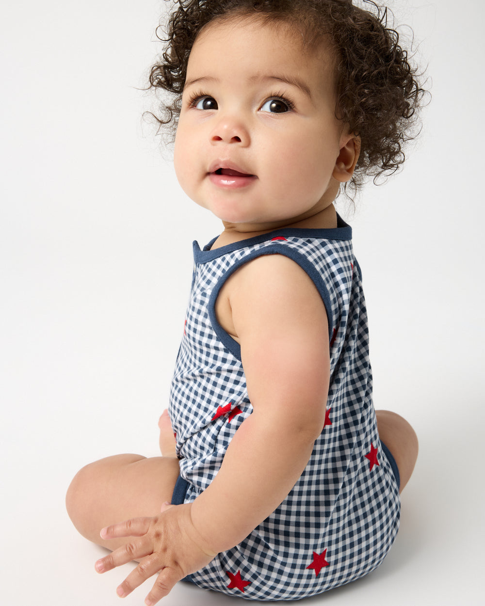 Back view of sitting baby wearing the Blue Ribbon Gingham Henley Romper
