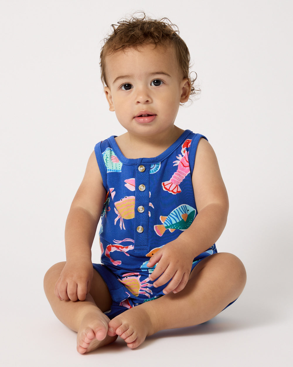 Sitting child wearing the Tidepool Party Henley Romper