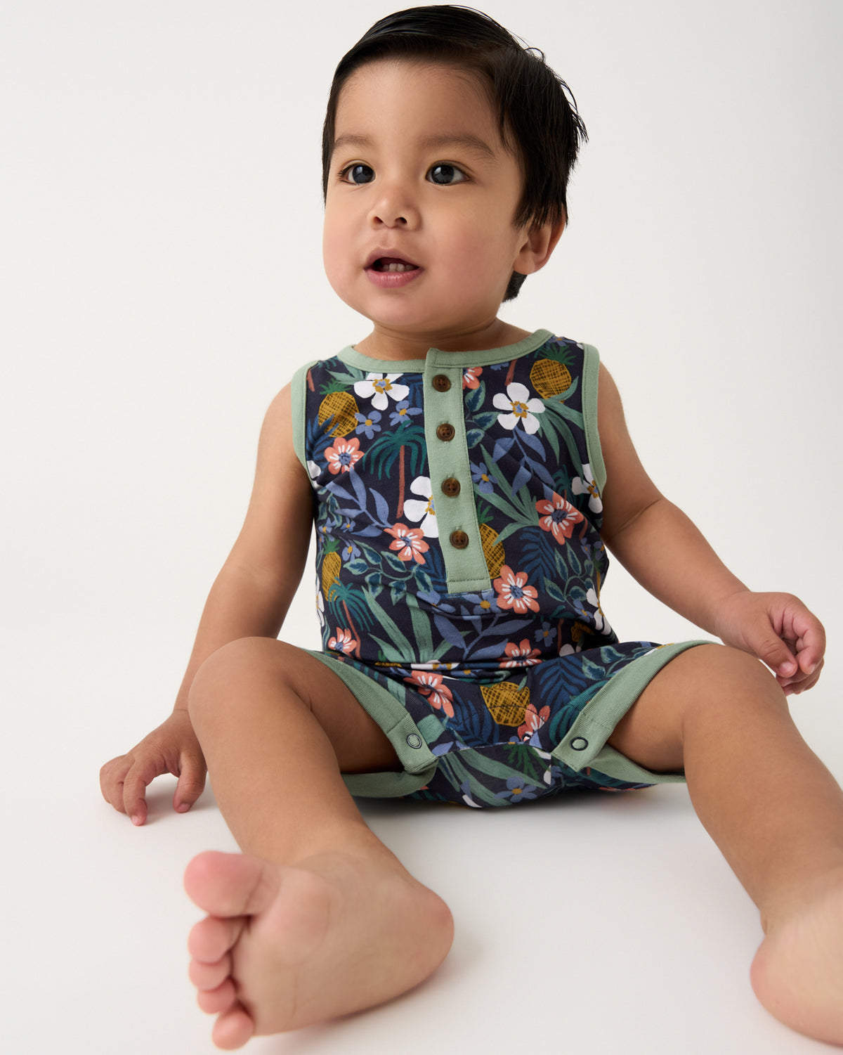 Sitting boy wearing the Tropical Garden Henley Romper