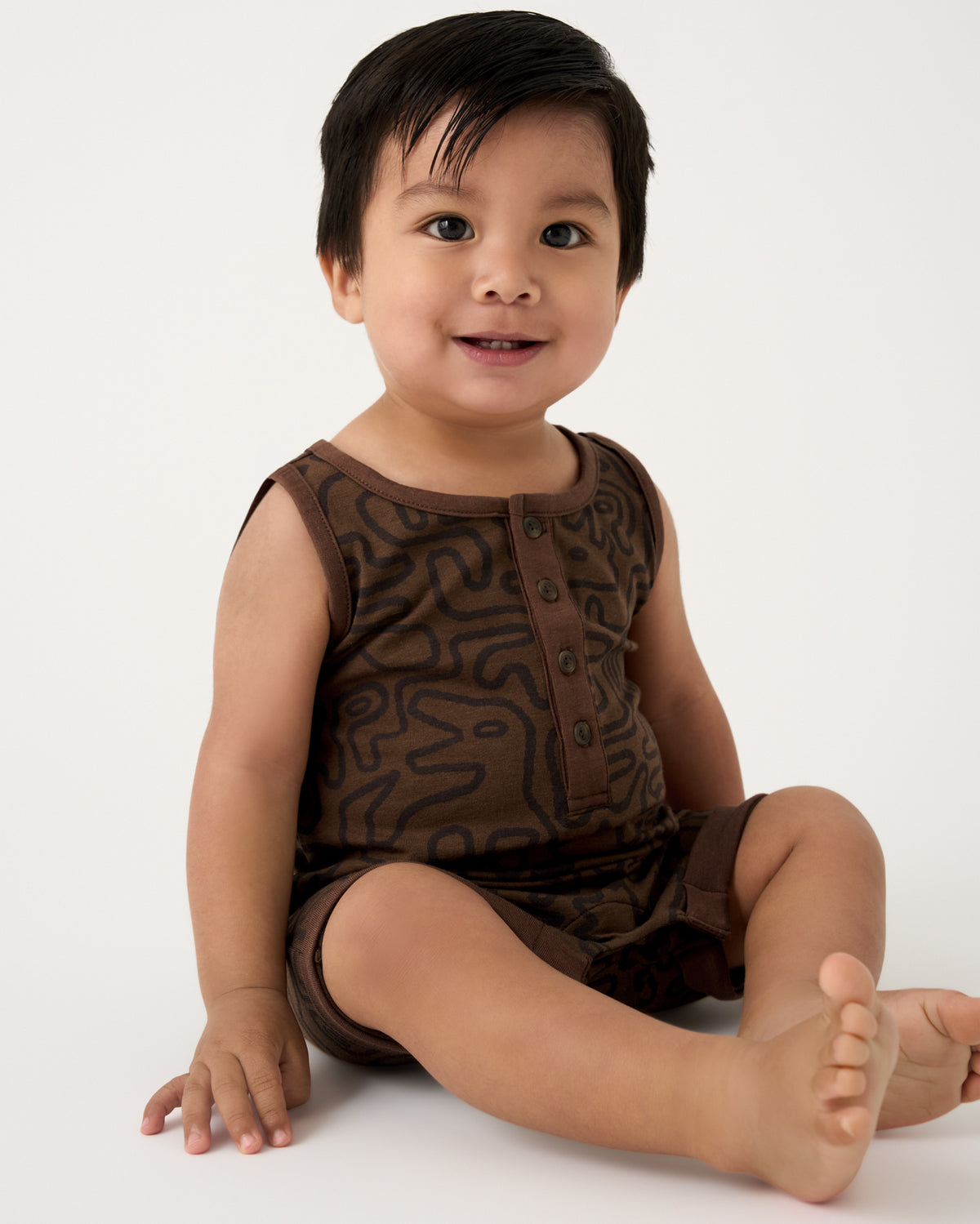 Sitting boy wearing the Dino Maze Henley Romper