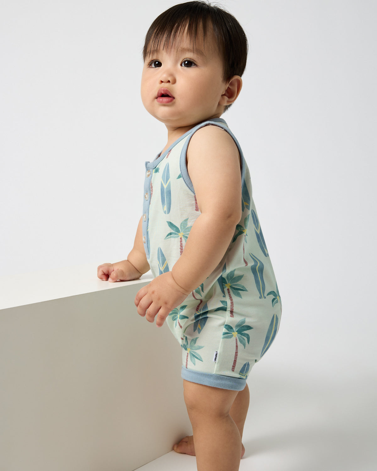 Standing baby wearing the Palm Dunes Tank Button Romper