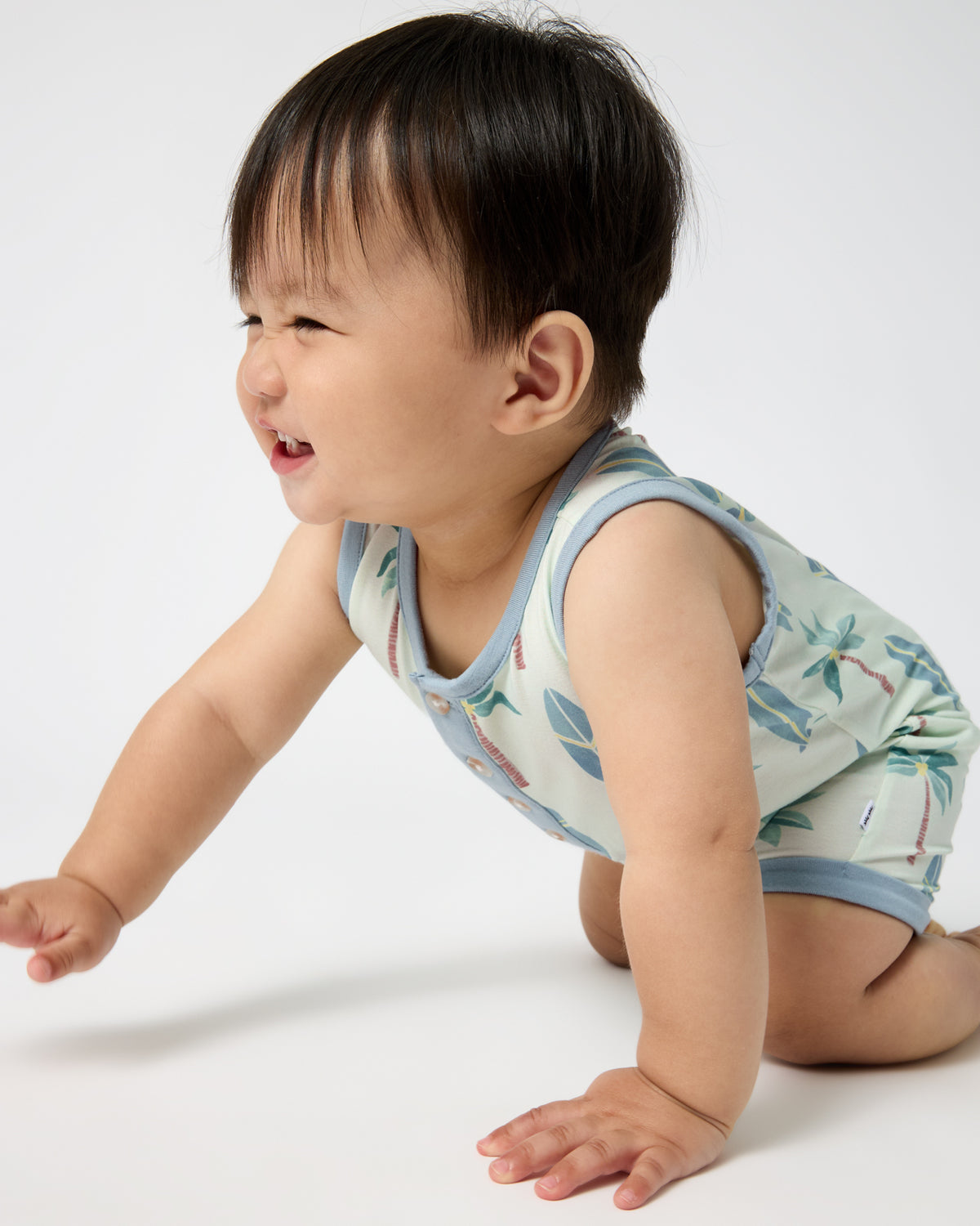 Crawling newborn wearing the Palm Dunes Tank Button Romper
