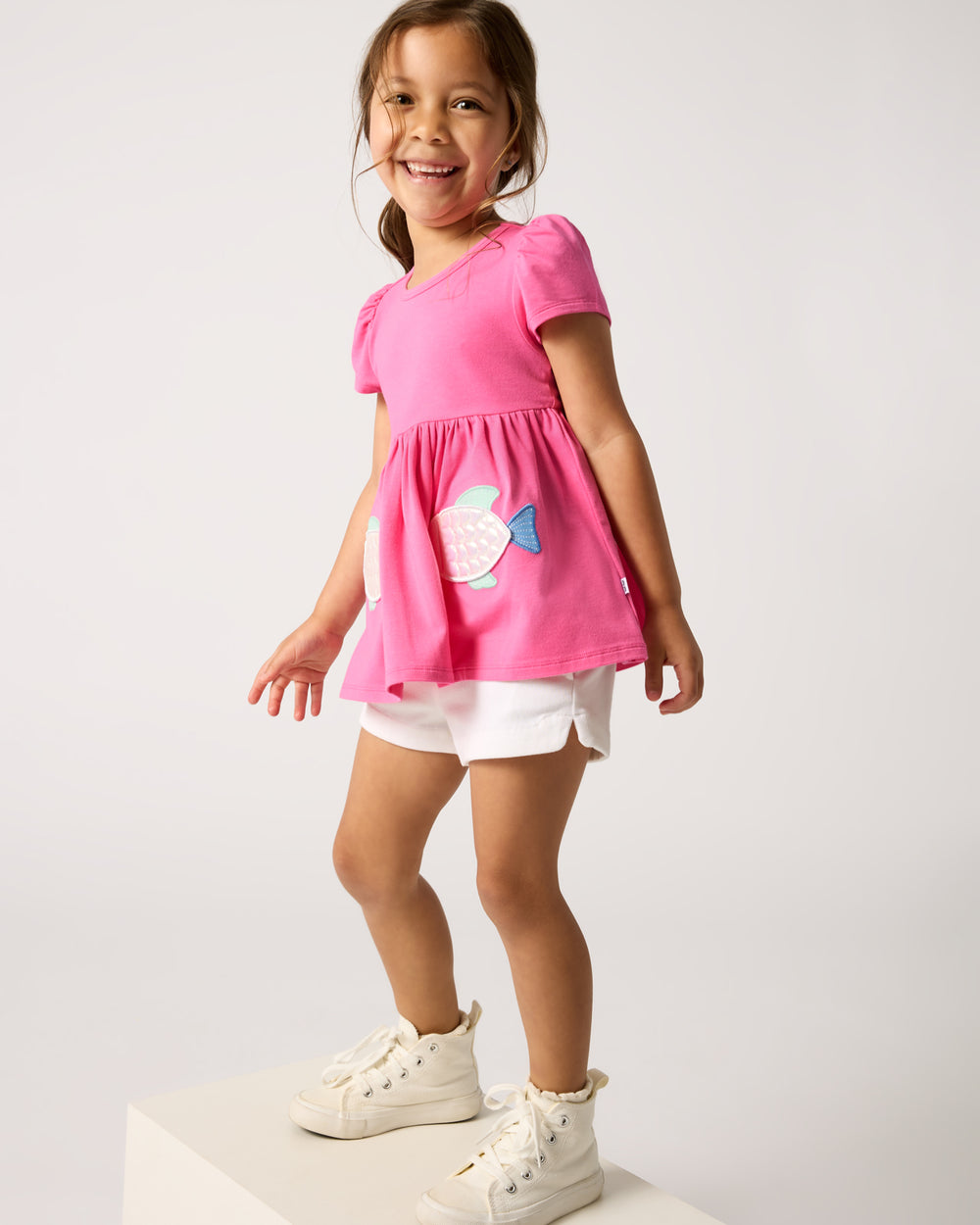 Girl wearing the Sparkling Scales Empire Tunic Top with white denim shorts