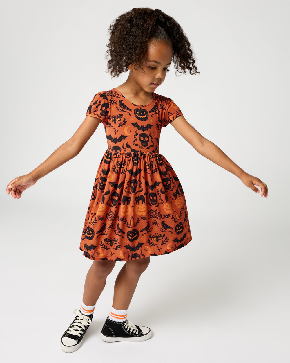 Girl wearing the Midnight Mischief Bow Back Skater Dress with black sneakers