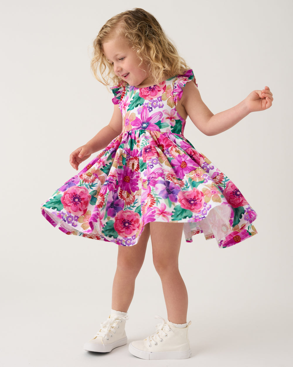 Twirling girl wearing the Hibiscus Blooms Tiered Flutter Dress with white sneakers