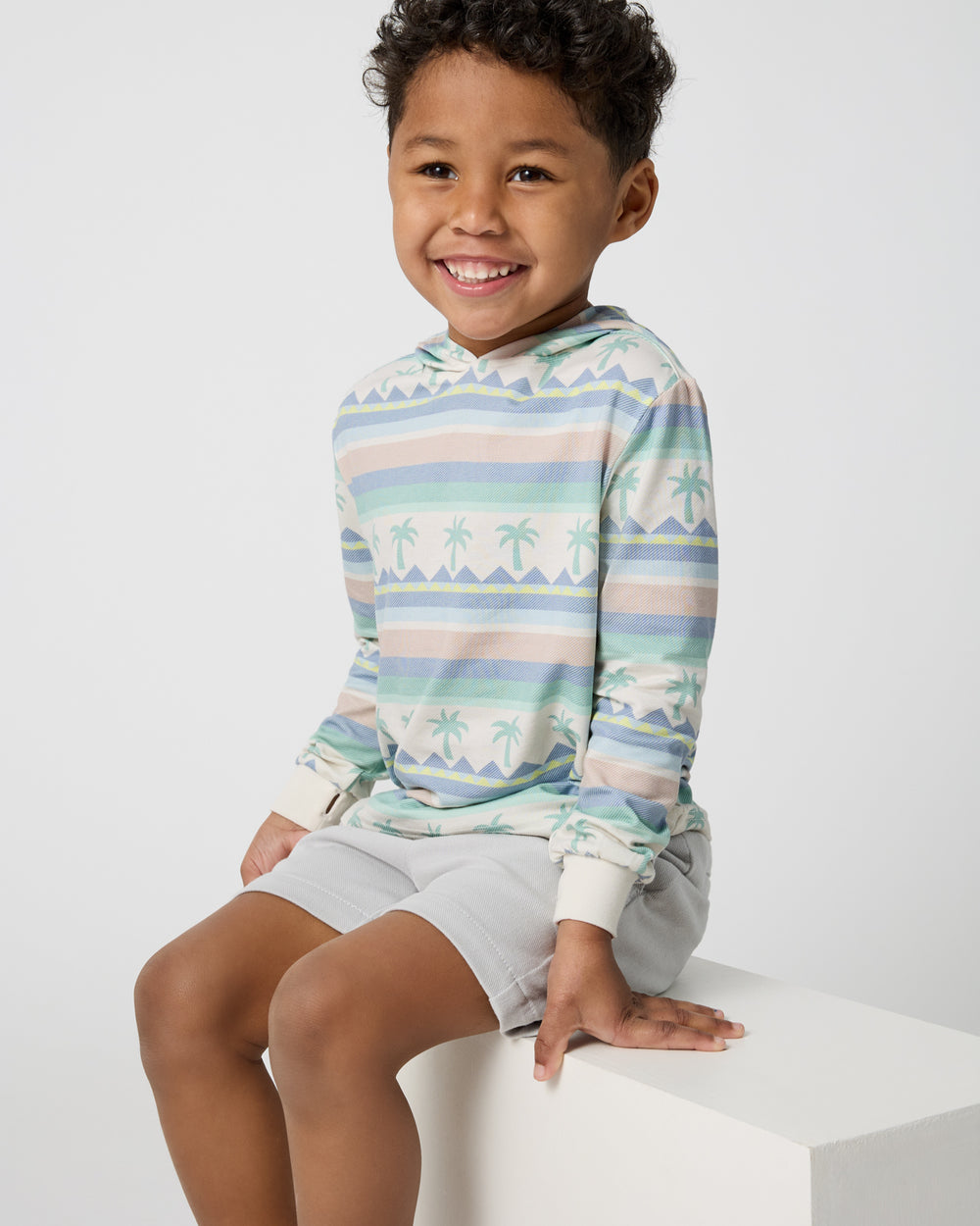 Sitting boy wearing the Swell Stripes Hooded Tee and Gray Boys Shorts