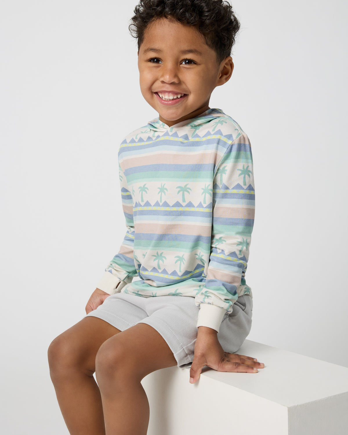 Sitting boy wearing the Swell Stripes Hooded Tee and Gray Boys Shorts