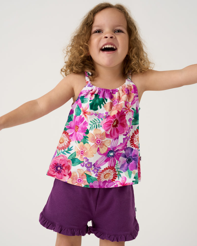 Posing girl wearing the Royal Violet Ruffle Shorts with the Hibiscus Blooms Bow Strap Tank