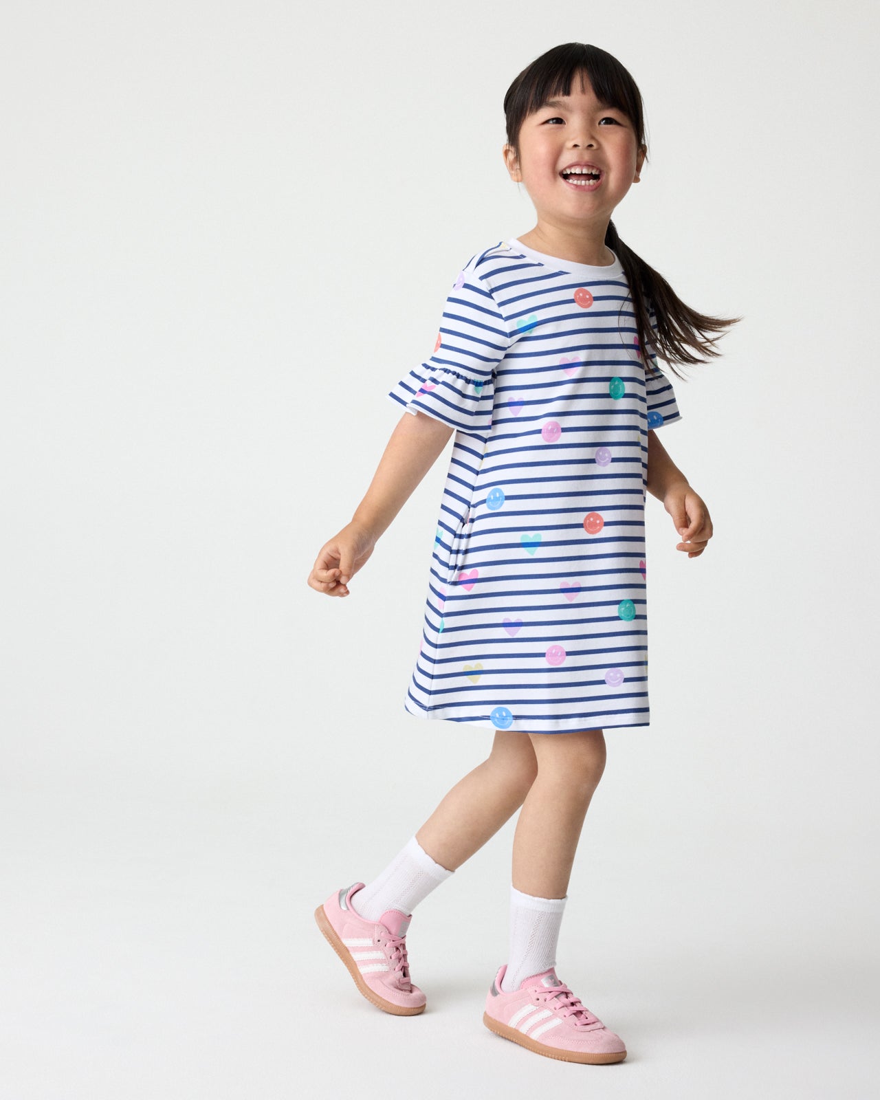 Girl wearing the Smiley Stripes Ruffled Shift Dress with pink sneakers