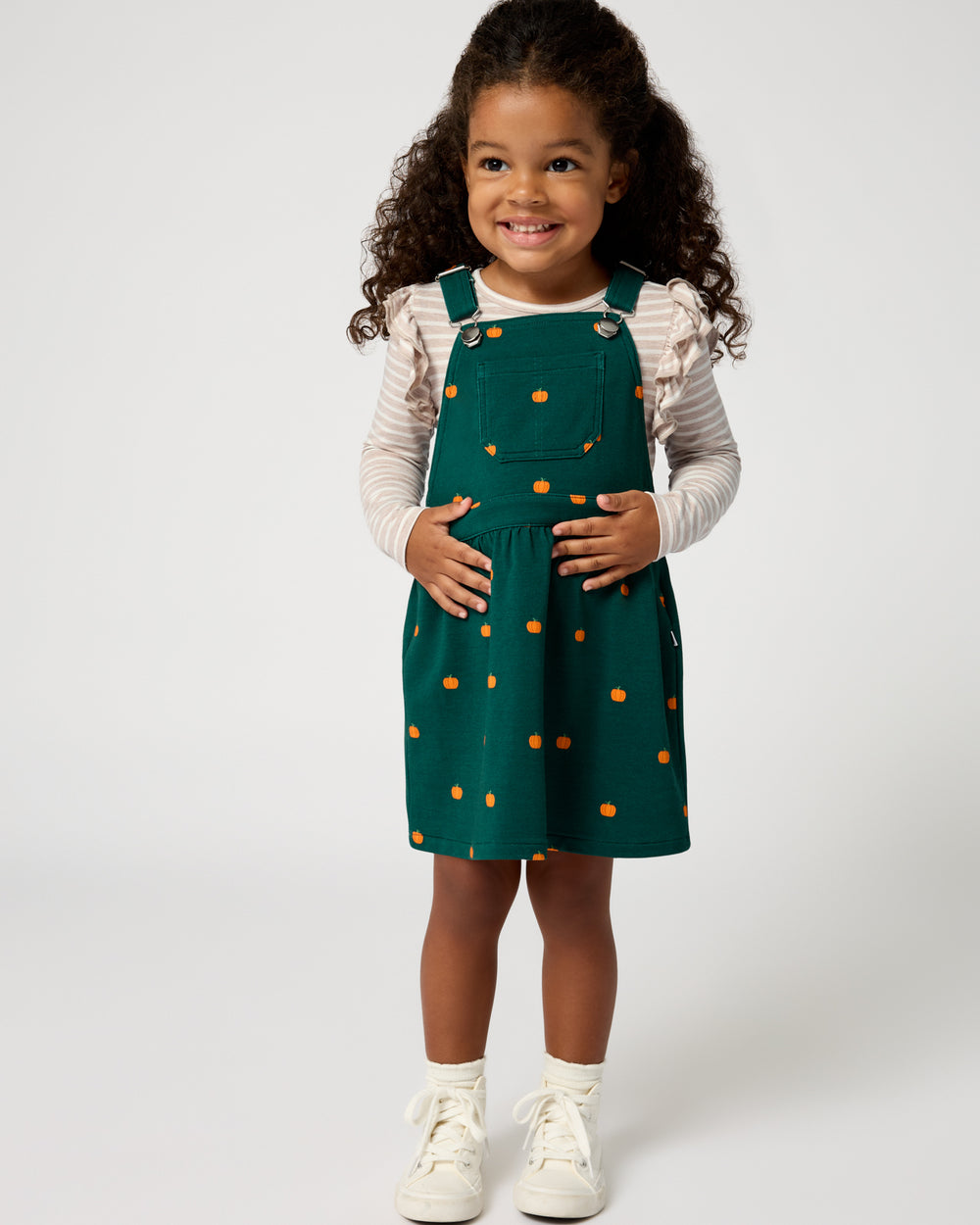 Standing girl wearing the Mini Pumpkins Skirt Overall Dress