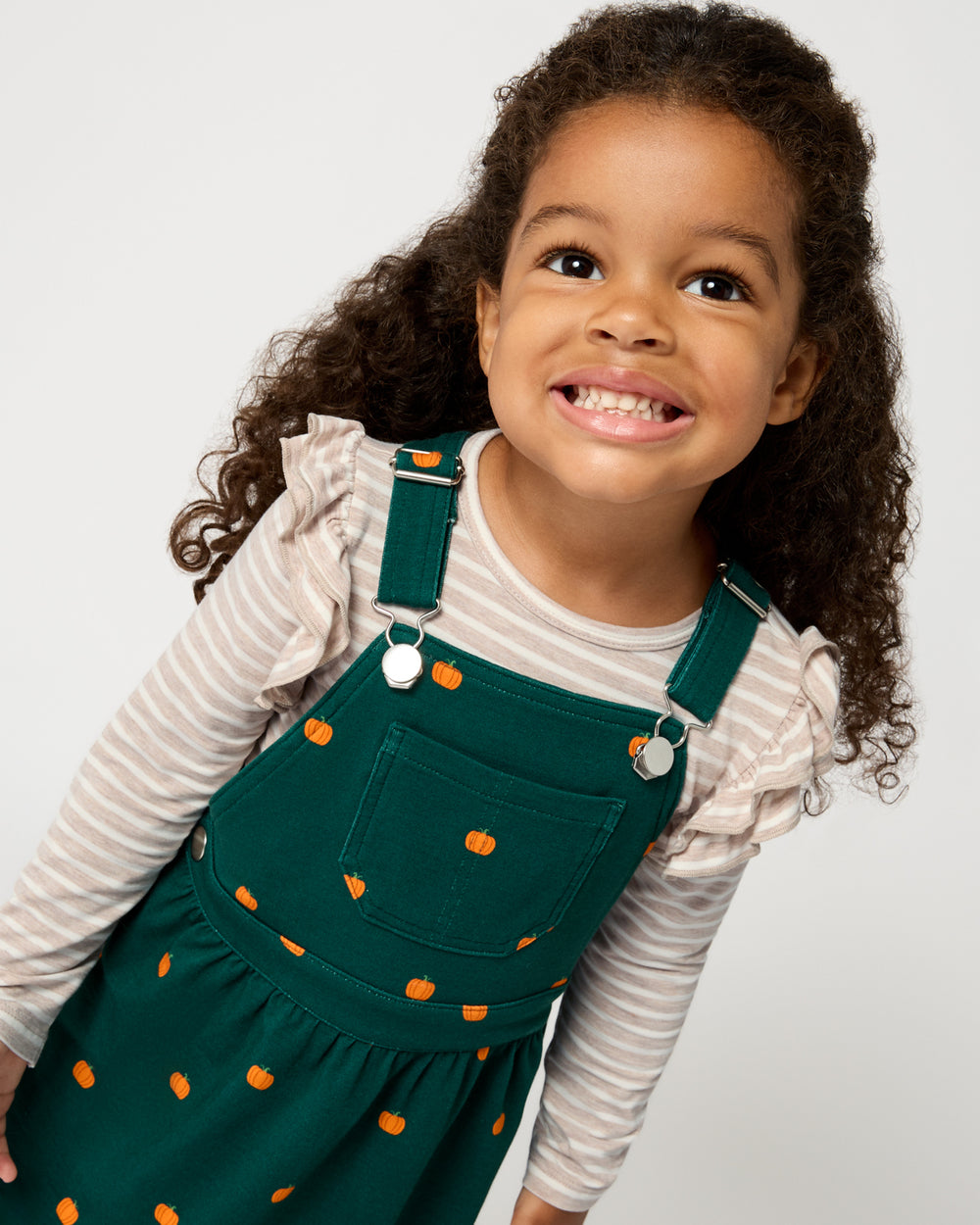 Close up of girl wearing the Mini Pumpkins Skirt Overall Dress over a ruffle tee