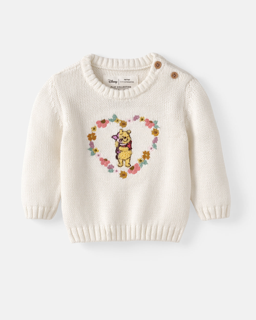 An off-white knit baby sweater featuring a central embroidered design of Winnie the Pooh surrounded by a floral heart, with two brown buttons on the shoulders.