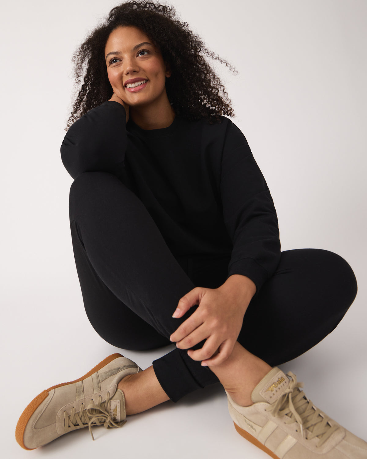 Sitting woman wearing the Black Women's Everyday Jogger with tan lifestyle sneakers
