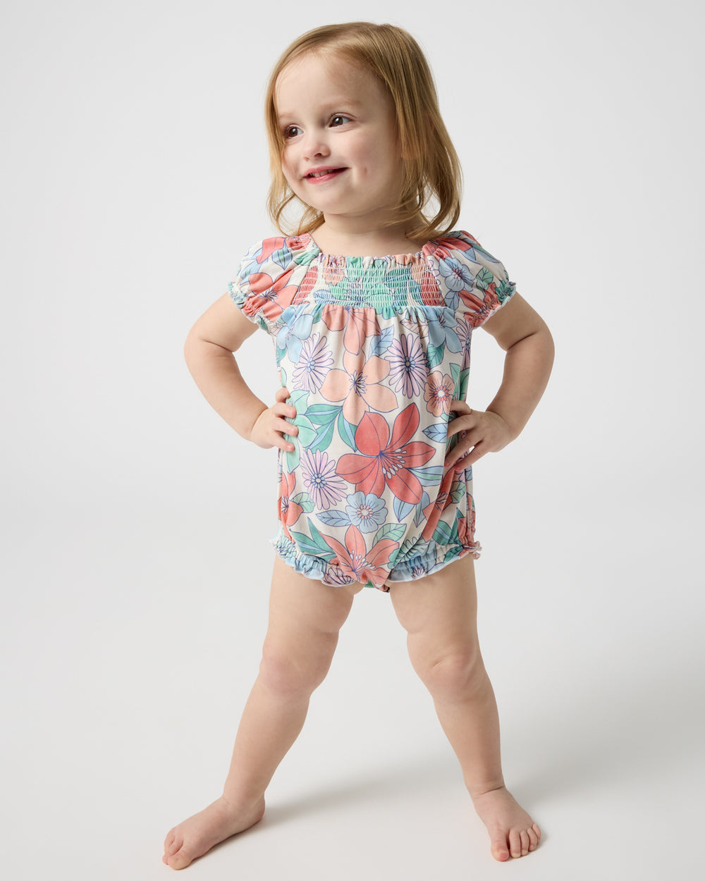 Standing toddler wearing the Shoreline Blooms Smocked Bubble Romper