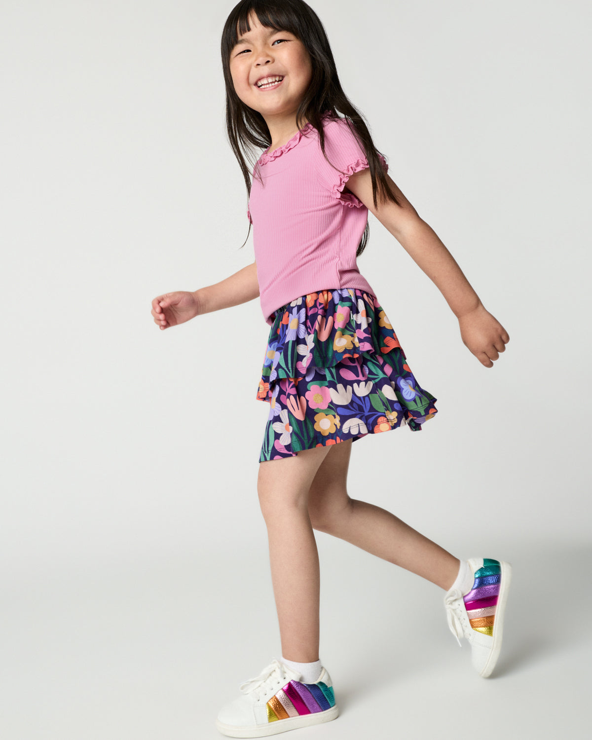 Walking girl wearing the Blush Orchid Ruffle Tee with a tiered floral skort